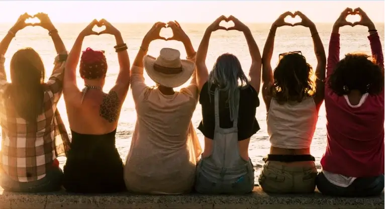 Plusieurs femmes assise de dos, levant les mains au ciel et formant un cœur avec leur doigts